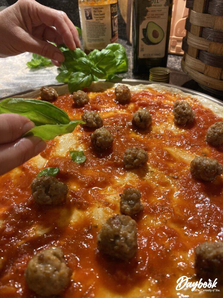 fresh basil being placed on a pizza