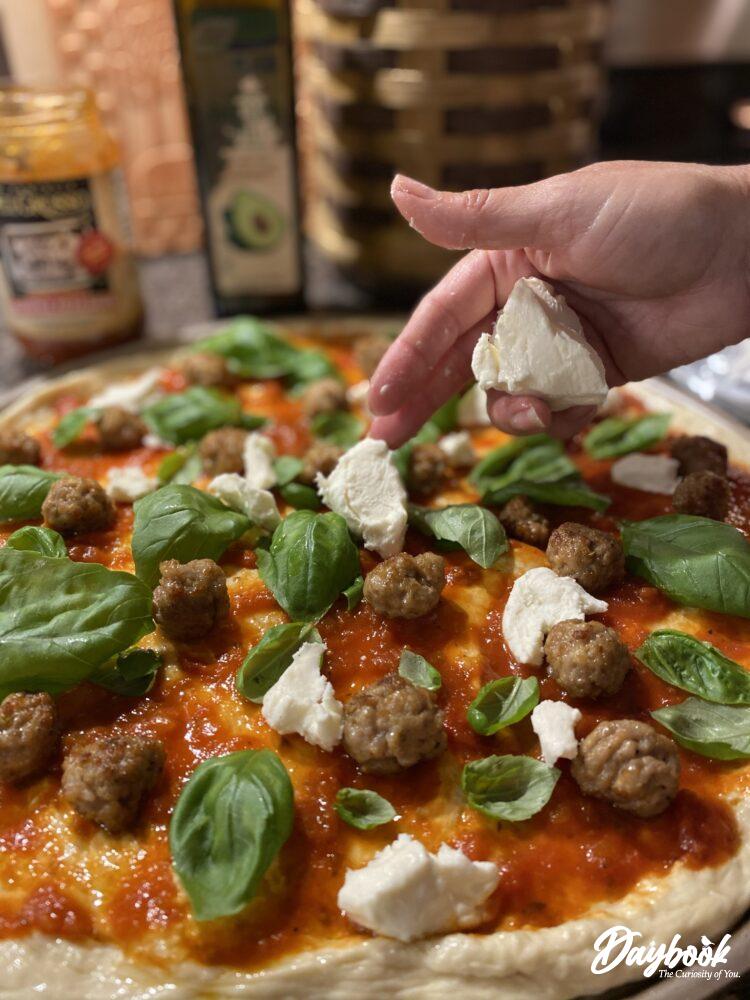 mozzarella cheese being placed on a pizza