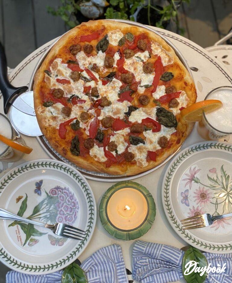 homemade pizza set on an outdoor table with plates and drinks