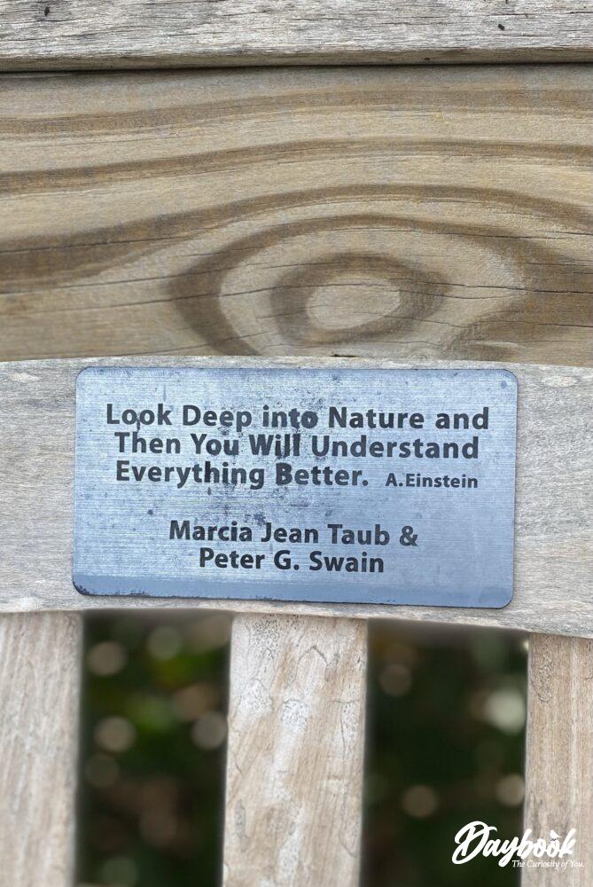 A park bench with a quote from Albert Einstein giving a reason to visit nature and a garden.
