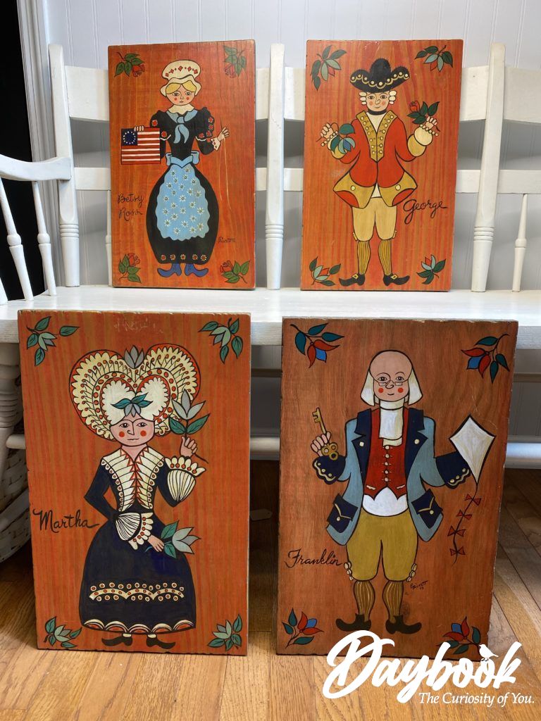 Four Americana folk art pieces displayed on a white bench