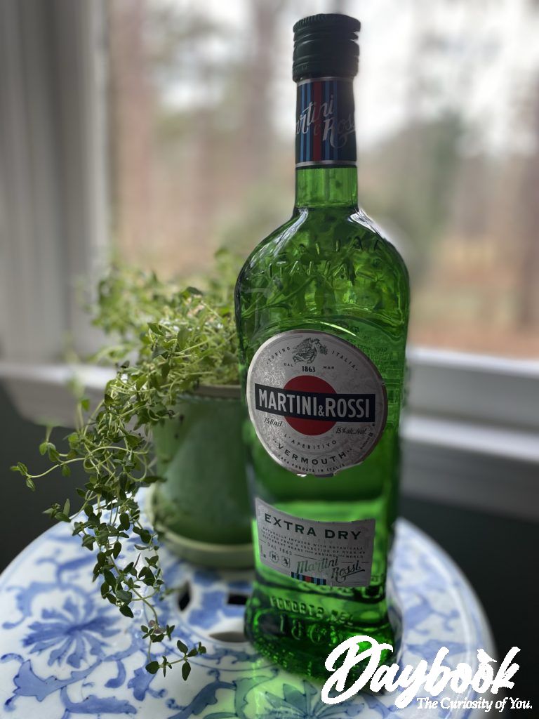 A green bottle of Martini & Rossi Dry Vermouth sitting on a small table in front of a window.
