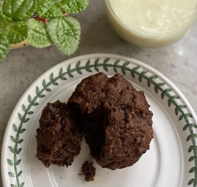 Triple chocolate banana muffin on a plate next to a glass of milk and a green plant