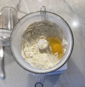 Food processor with cookie crumble mix and a raw egg ready to blend