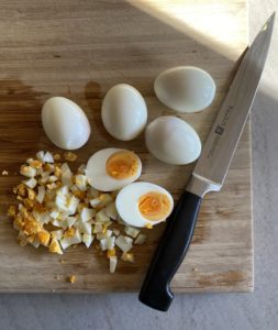 Six boiled eggs on a cutting board with one chopped and one cut in half.