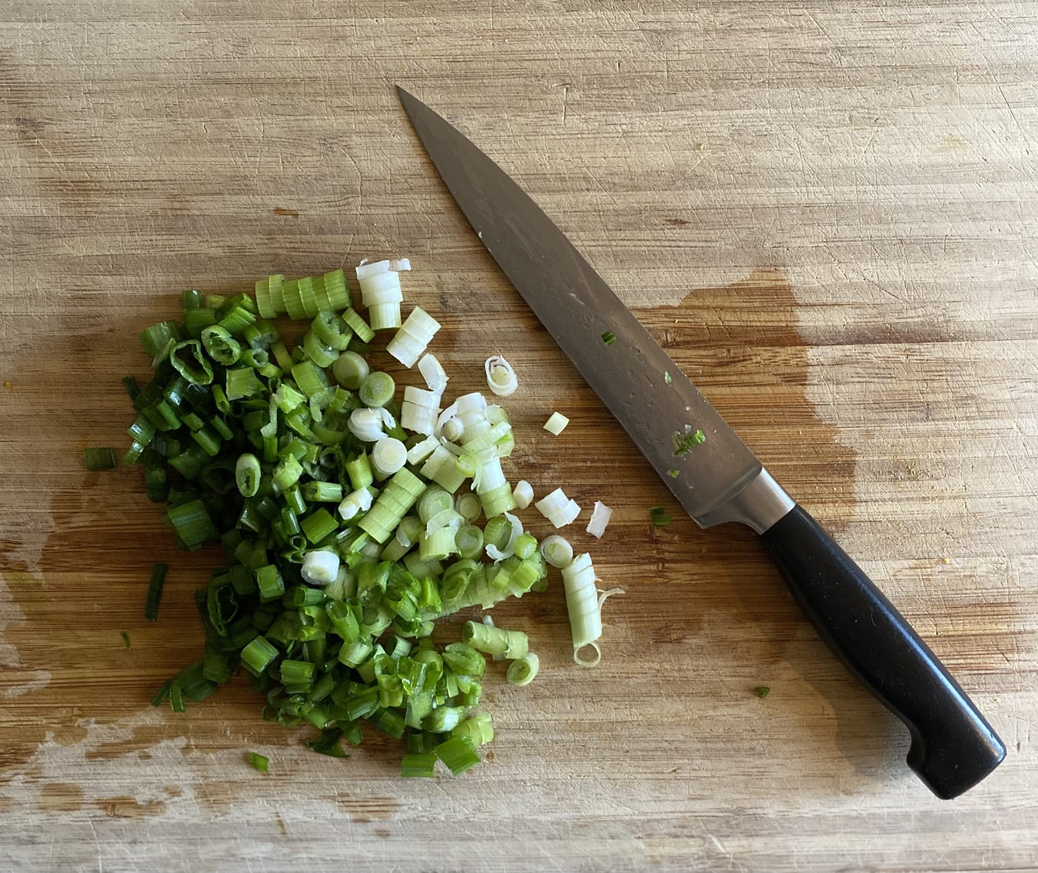 Six scallions chopped on a wooden cutting board.