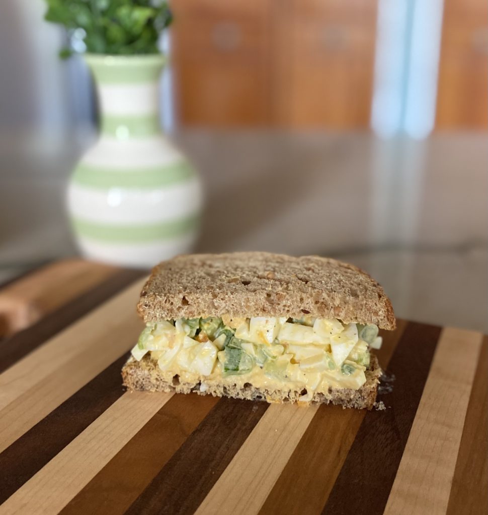 Half of a simple egg salad sandwich on a wooden cutting board.