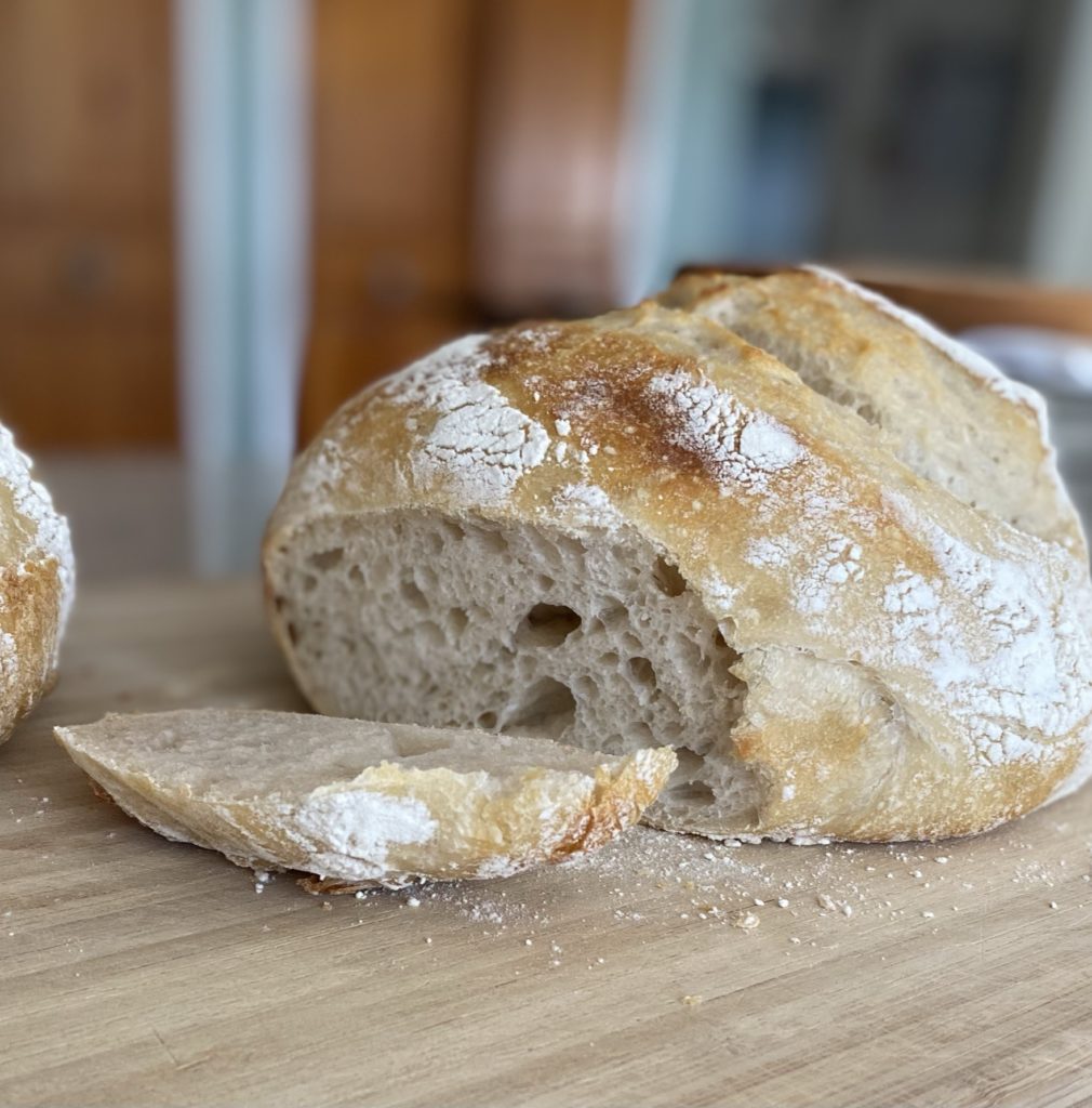 A loaf of sourdough bread being sliced on a cutting board.