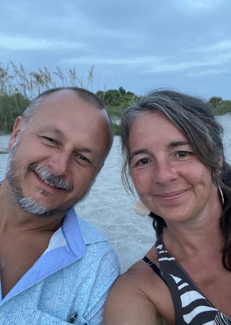 A man and a woman sitting on the beach at sunset.