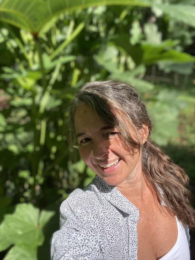 Kristy standing under a large okra leaf.