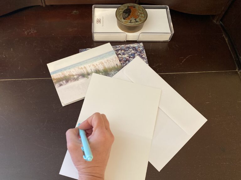 A hand holding a pen ready to write a letter on a white card