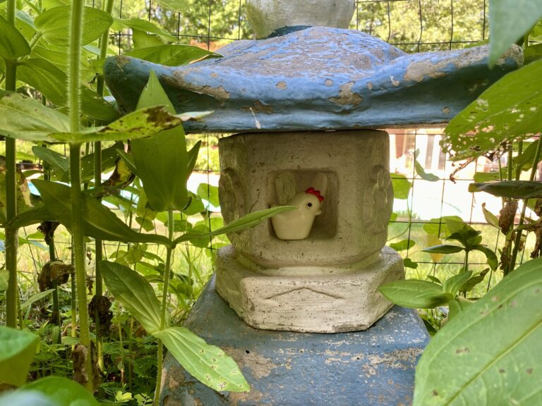 A blue and white concrete pagoda hidden in a garden on a sunny day.
